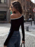 Back view of black off-shoulder top, highlighting asymmetrical design with white accent, paired with denim
