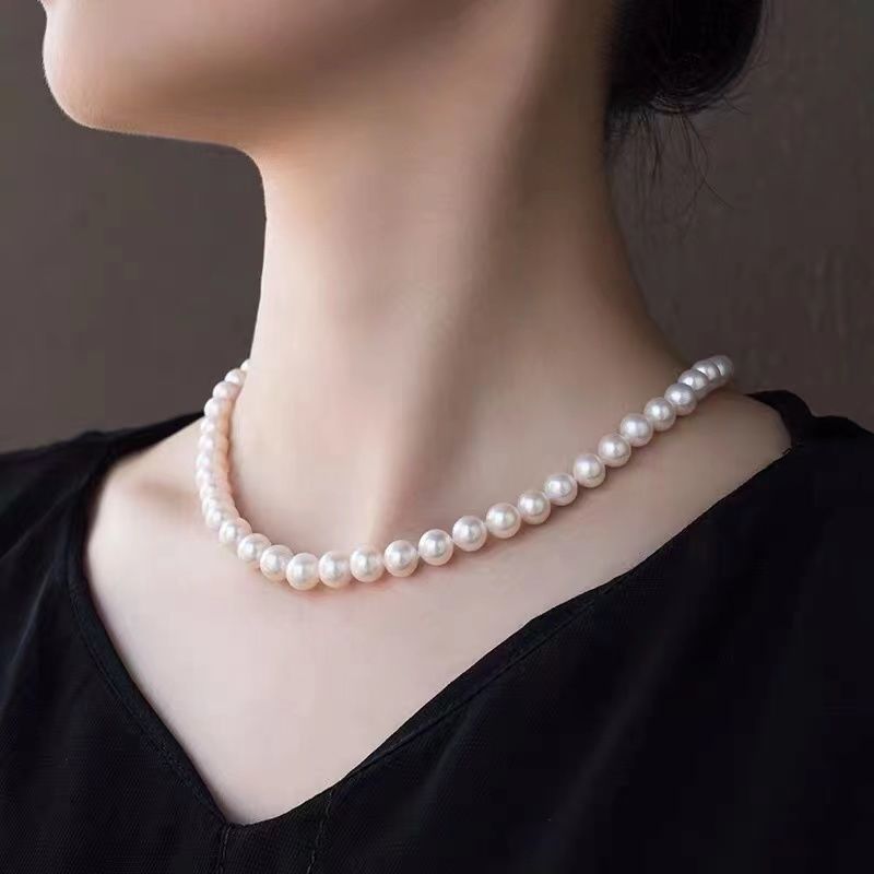 Classic white pearl necklace worn on neck with black top, showing lustrous single strand design