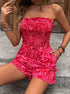 Woman wearing a red strapless romper with a tropical leaf print, sitting on stairs with one hand on her lap.