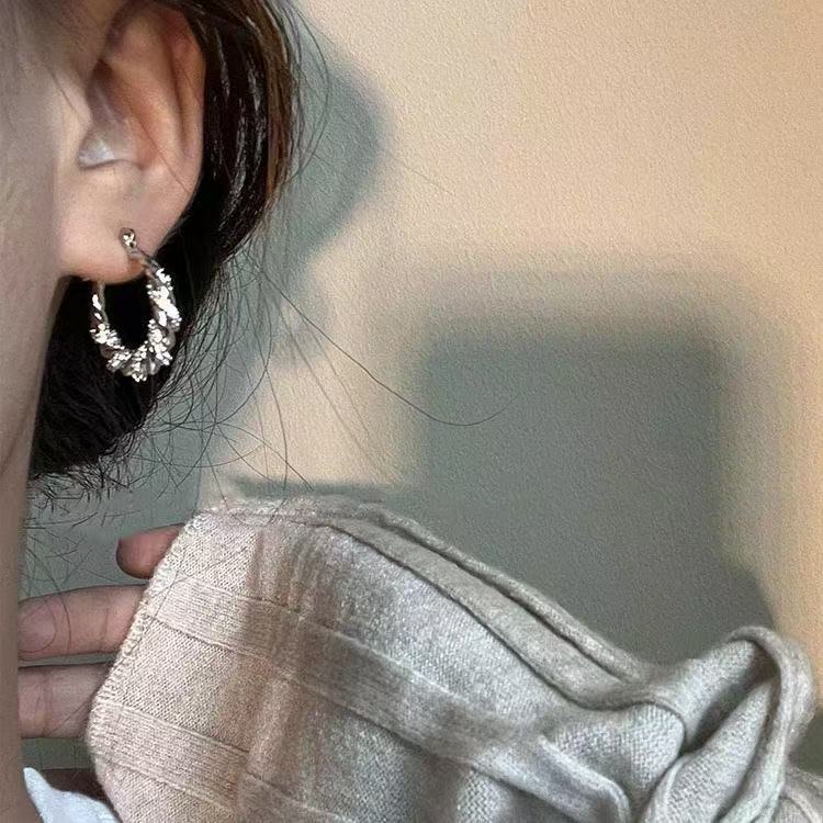 Silver textured hoop earring with crystal detailing worn with light-colored sweater