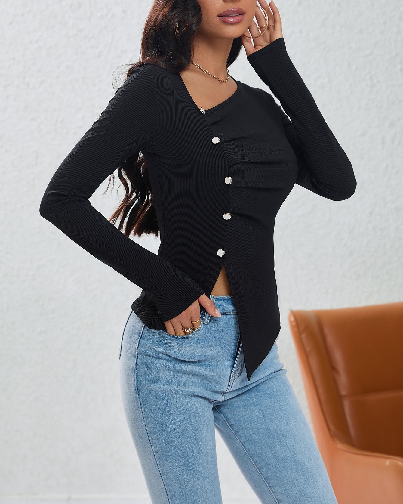 Side view of fitted black button-front top with ruched detail and asymmetric hem worn with denim