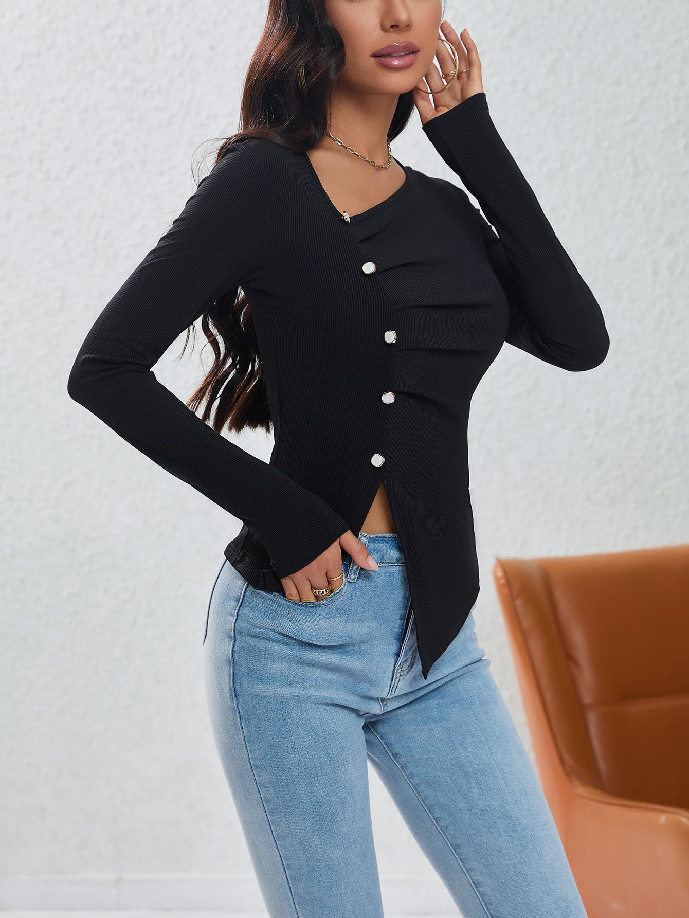 Side view of fitted black button-front top with ruched detail and asymmetric hem worn with denim