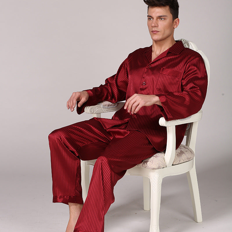 Man seated in white chair wearing burgundy striped silk pajamas with chest pocket and relaxed fit bottoms