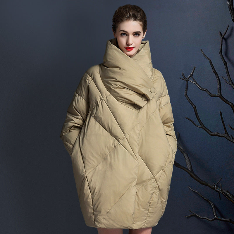 Model wearing beige quilted puffer coat with oversized high collar and button closure against dark blue background