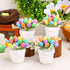 A white pot filled with artificial green leaves and vibrant, multicolored speckled eggs arranged in a floral shape, placed on a table with a festive background.