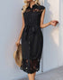Woman wearing a black button-up midi dress with lace inserts on the chest and hem, a tied waist belt, and cap sleeves, holding a straw hat.