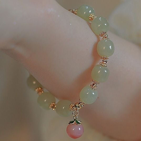 Close-up of a jade and gold bracelet with a pink cherry charm, elegantly draped on a wrist