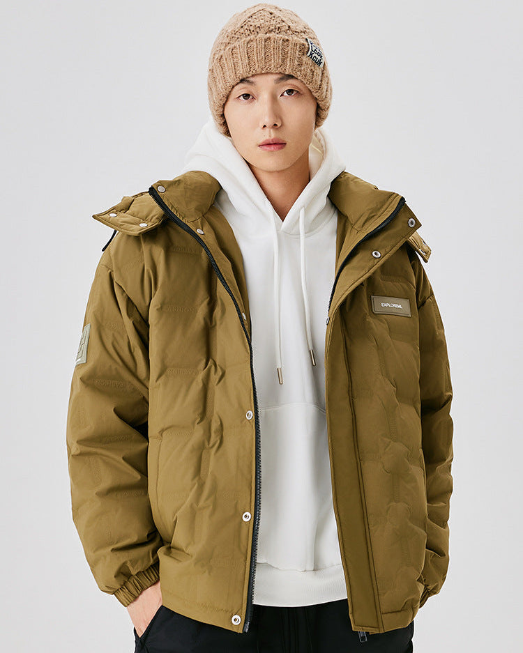 A man wearing a beige knit beanie and olive puffer jacket over white hoodie, posing against white background