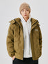 A man wearing a beige knit beanie and olive puffer jacket over white hoodie, posing against white background