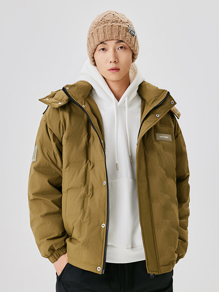A man wearing a beige knit beanie and olive puffer jacket over white hoodie, posing against white background