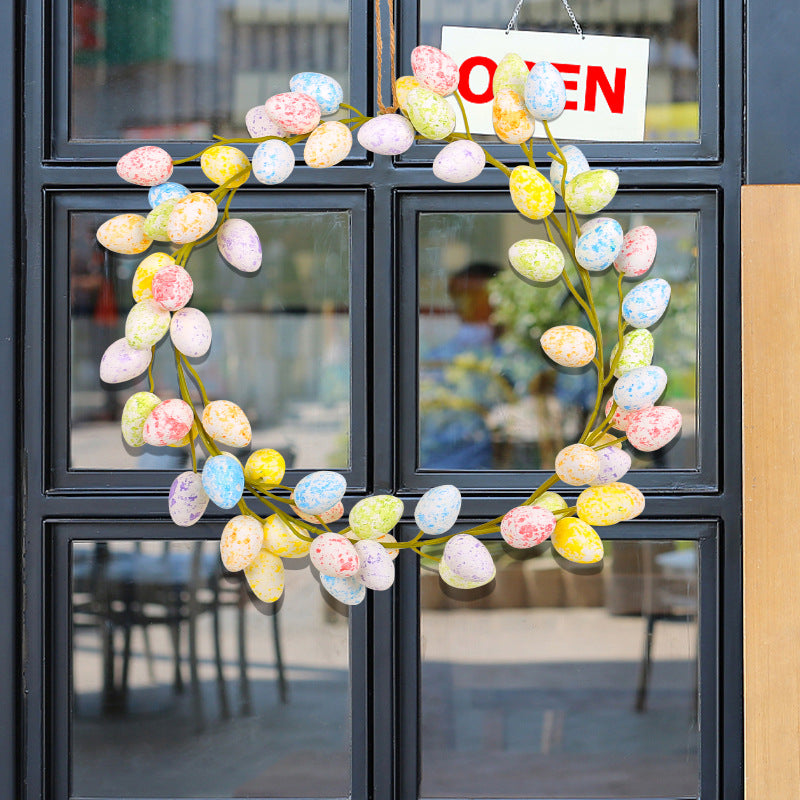 A colorful Easter egg wreath hanging on a glass door with an "OPEN" sign, reflecting an outdoor café setting.
