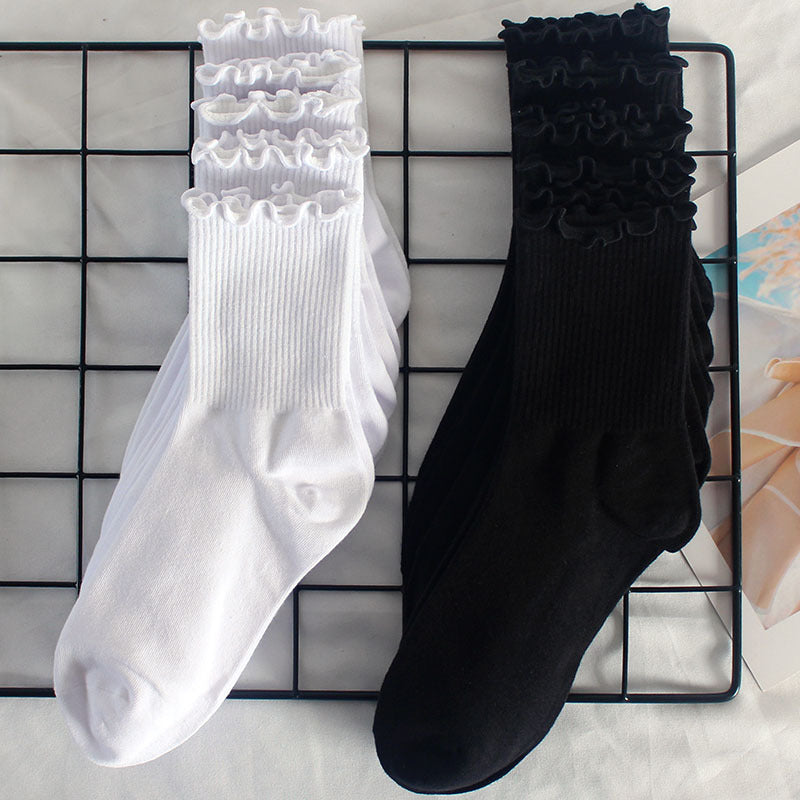 White and black ruffle-trim ankle socks displayed side by side on a metal grid rack, featuring ribbed cuffs and soft cotton material