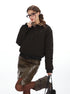 A woman wearing a black quilted bomber jacket with leopard print collar touching her lip playfully, styled with a brown leather skirt and glasses against white backdrop
