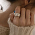 Woman wearing silver crumpled-effect ring, shown with cozy white knit sweater and blue nail polish