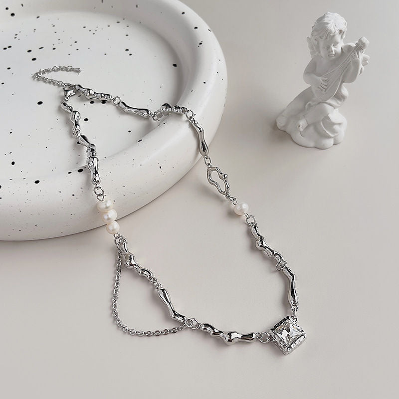 Silver branch-link necklace with pearls and a square gemstone pendant on a ceramic tray