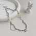 Silver branch-link necklace with pearls and a square gemstone pendant on a ceramic tray