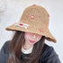 Woman wearing a woven straw bucket hat with embroidered apple details and a fabric label, covering part of her face.