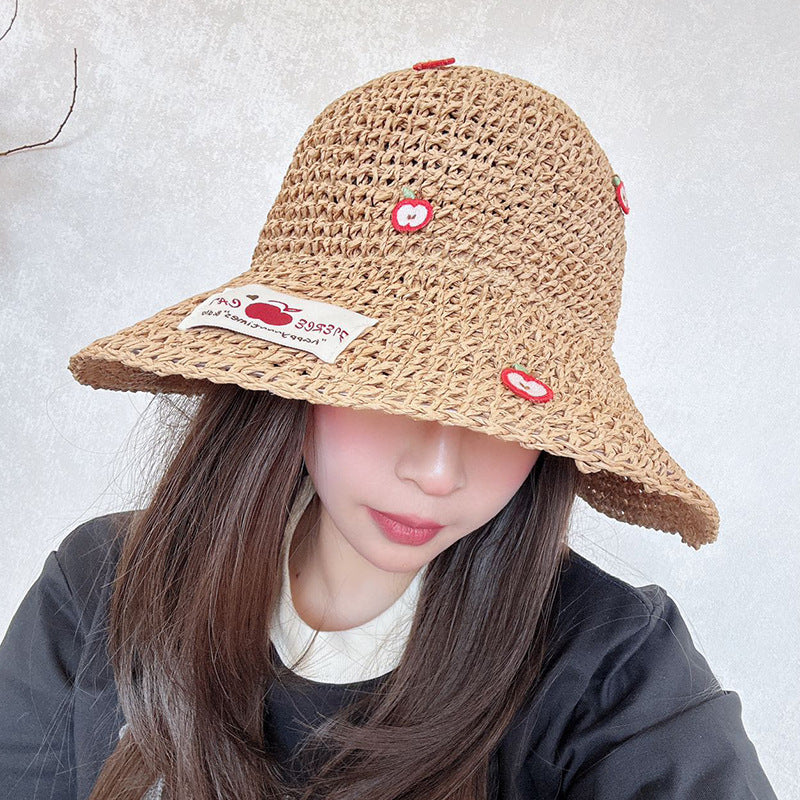 Woman wearing a woven straw bucket hat with embroidered apple details and a fabric label, covering part of her face.