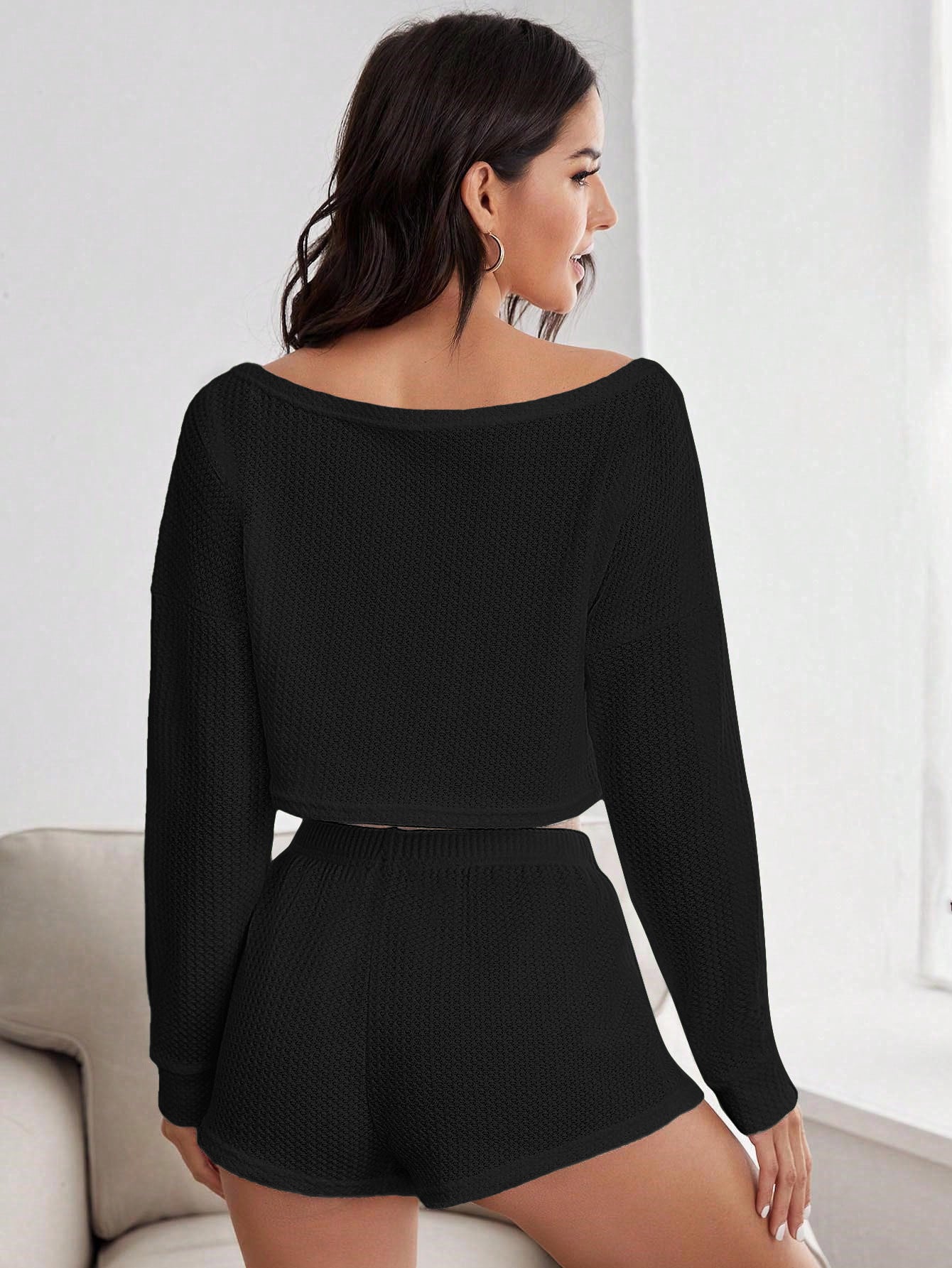 Back view of woman in black textured loungewear set showing off-shoulder design and shorts