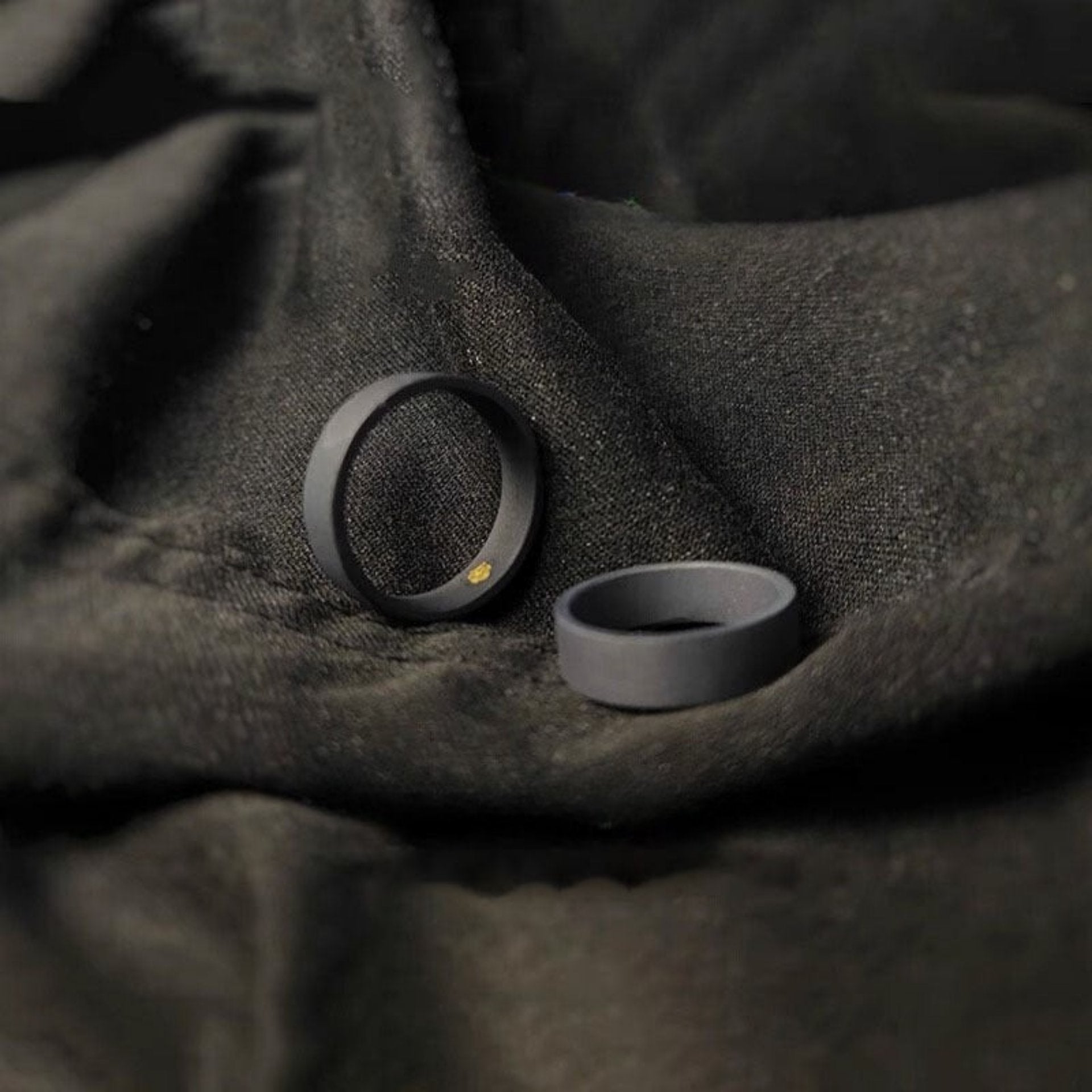  Two matte black rings with a minimalist design, placed on a dark fabric background with gold Chinese text above.