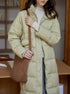 Light beige long puffer coat with brown shoulder bag, cream turtleneck sweater and dark jeans, indoor setting