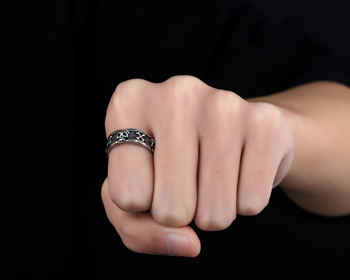 A close-up of a clenched fist wearing a silver skull-patterned ring against a black background, highlighting the intricate design.
