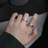 A person wearing silver adjustable Roman numeral rings on two fingers, showcasing vintage style jewelry against grey fabric