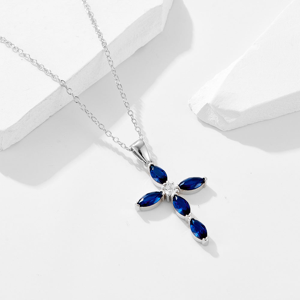 A silver cross pendant with blue marquise sapphires and center diamond on delicate chain against white backdrop