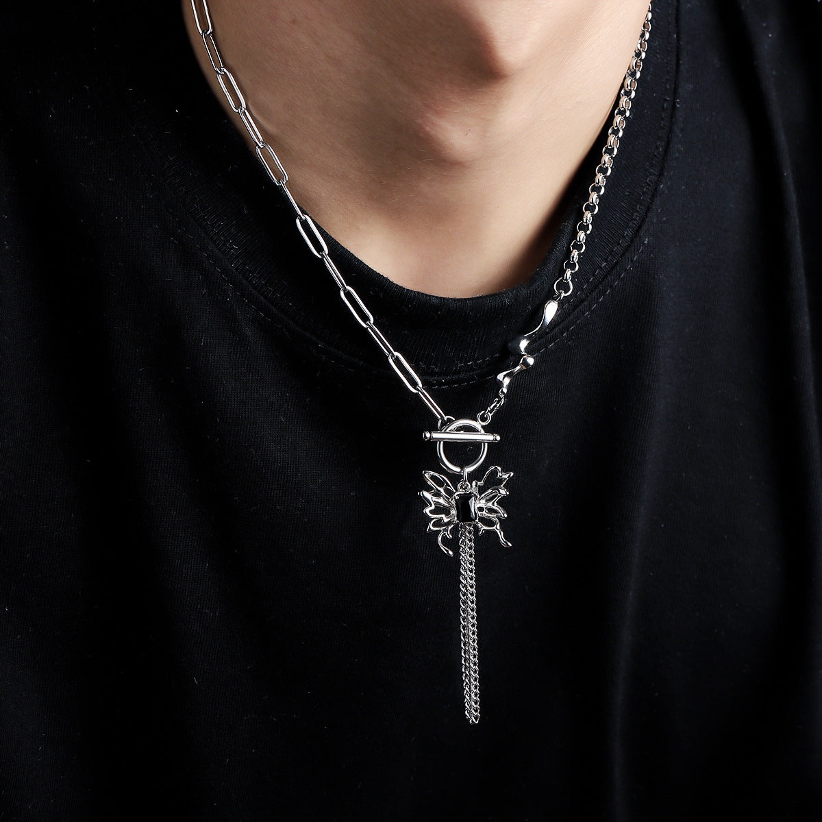 Titanium Steel asymmetric necklace featuring paperclip chain and rolo chain combination, toggle clasp, and butterfly pendant with dangling chain tassels, styled on model wearing black t-shirt