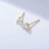 Gold three-prong diamond stud earrings with small round brilliant stones on white surface casting soft shadow