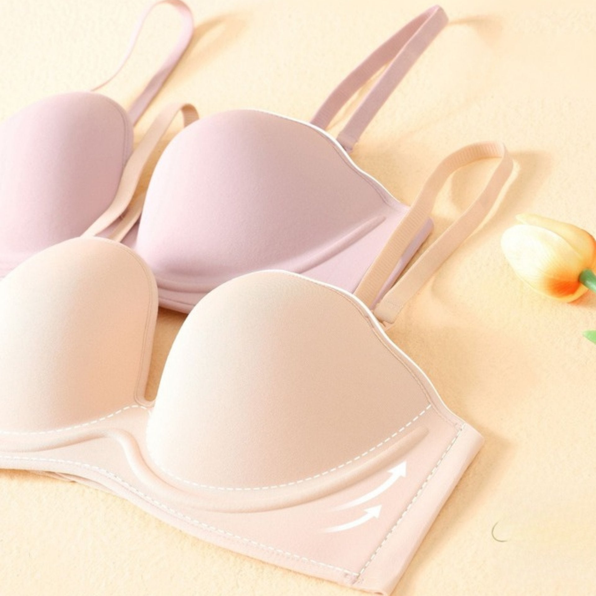 Two seamless padded bras in medium nude and pink, featuring soft underwire support and breathable fabric, displayed on a pastel background with a tulip.