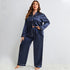 Model in navy blue silk pajama set with white piping trim, wearing crystal necklace against white background