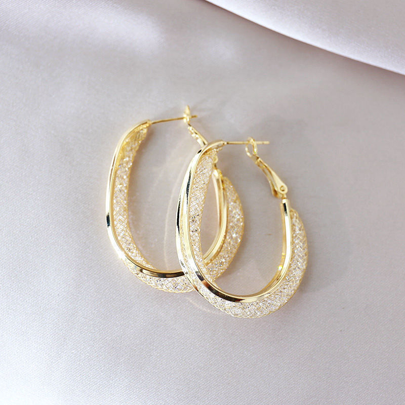 Gold-plated oval hoop earrings with crystal mesh inlay on white fabric background