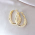 Gold-plated oval hoop earrings with crystal mesh inlay on white fabric background