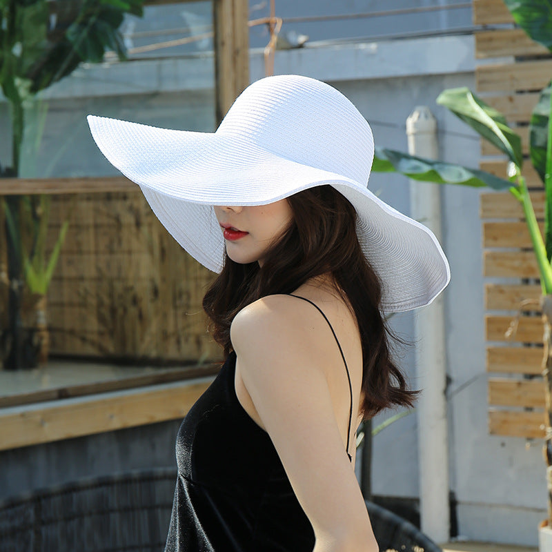 Woman wearing a wide-brimmed white sun hat with a floppy design, paired with a black spaghetti-strap dress outdoors.