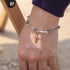 A silver bone-link bracelet with a gold cross pendant, worn on a wrist against an outdoor background.