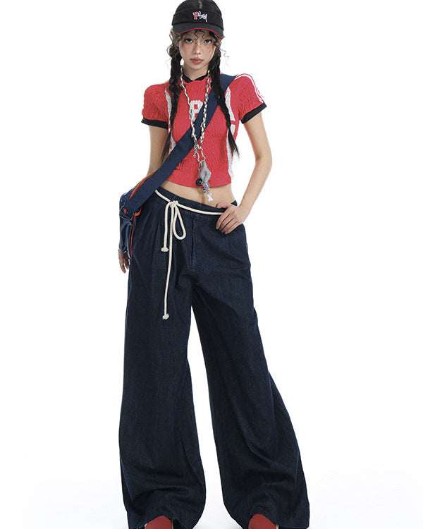 Woman wearing dark wide-leg drawstring jeans with a red crop top and cap.