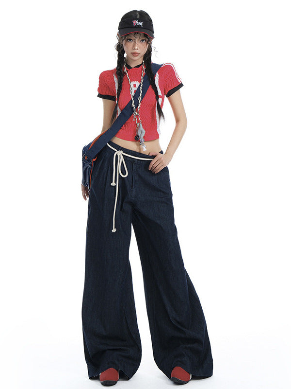 Woman wearing dark wide-leg drawstring jeans with a red crop top and cap.