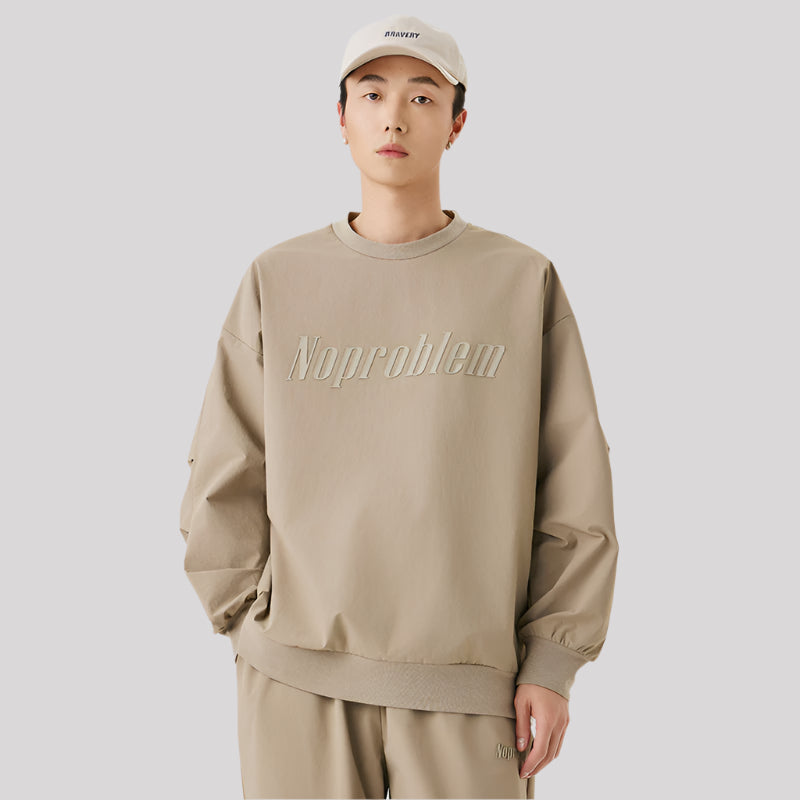 Male model wearing a beige oversized sweatshirt with "NoProblem" embossed on the chest, paired with matching sweatpants and a baseball cap
