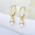 Gold huggie hoop earrings with double diamond drop charms, featuring small crystals in prong settings on white surface