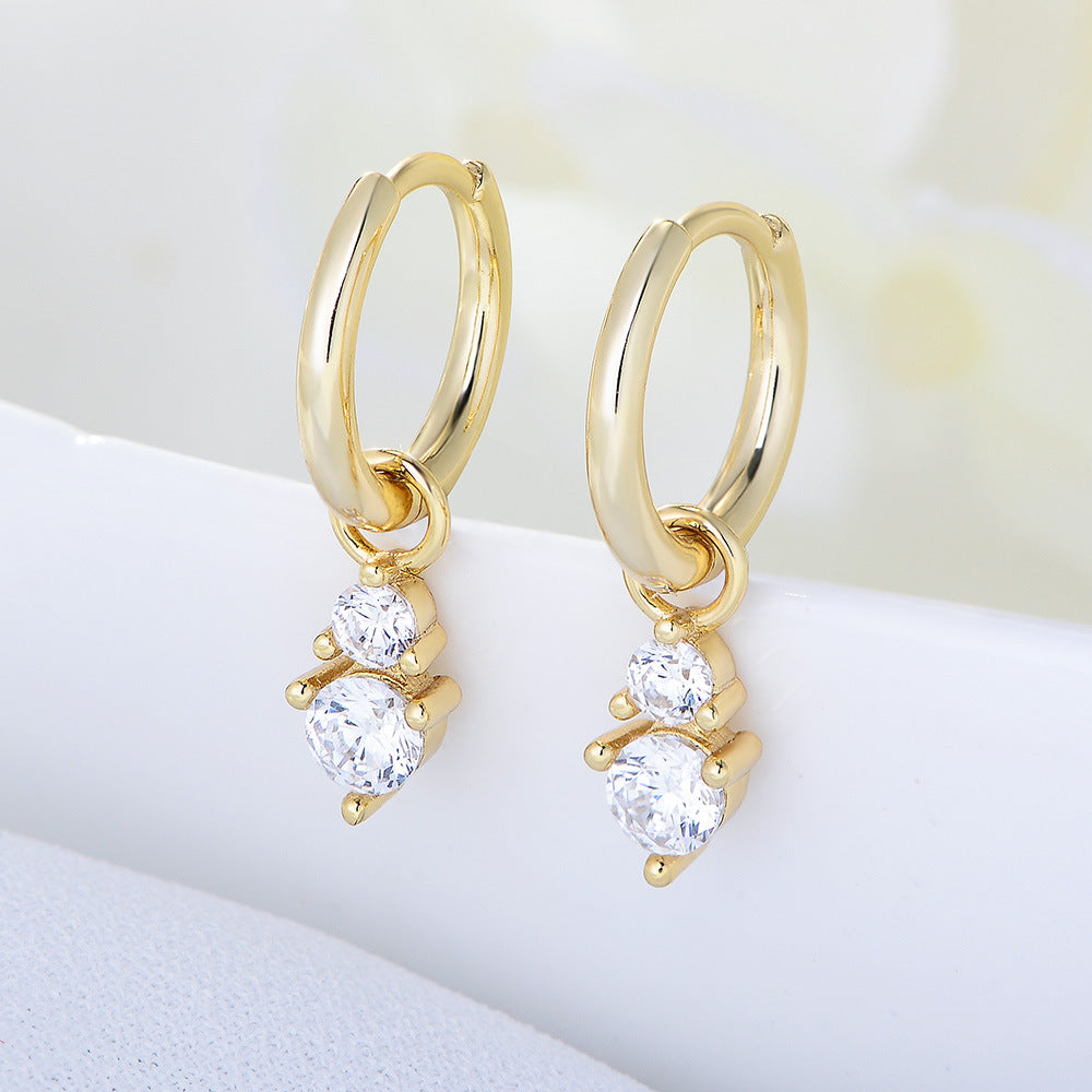 Gold huggie hoop earrings with double diamond drop charms, featuring small crystals in prong settings on white surface