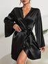 A woman wearing a black silk robe with lace trim V-neck, bell sleeves, and waist tie, showing white manicured nails