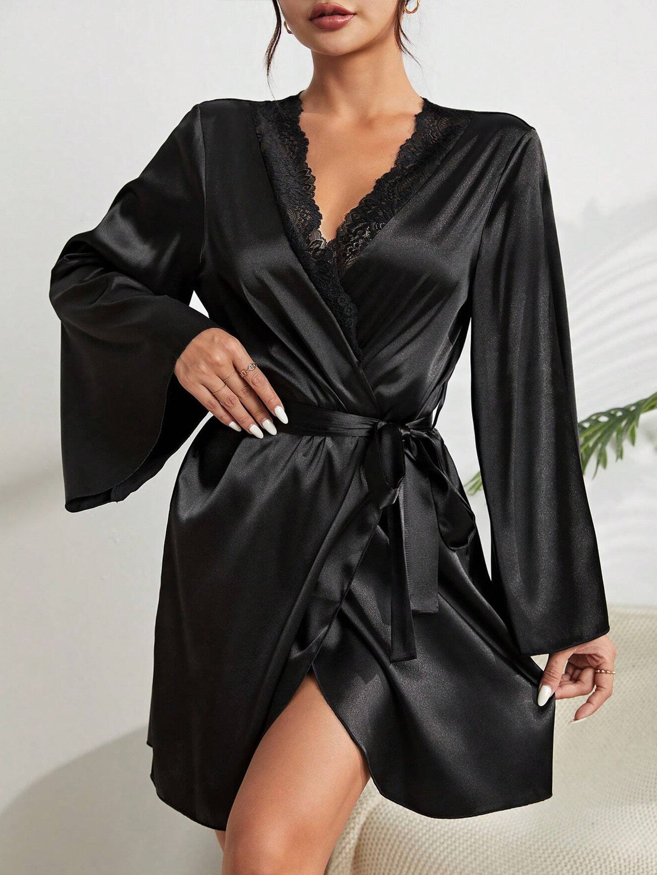 A woman wearing a black silk robe with lace trim V-neck, bell sleeves, and waist tie, showing white manicured nails
