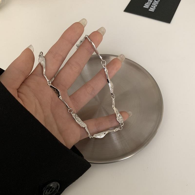 Silver textured chain necklace held in a hand over a metallic dish, showcasing its intricate design