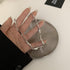 Silver textured chain necklace held in a hand over a metallic dish, showcasing its intricate design