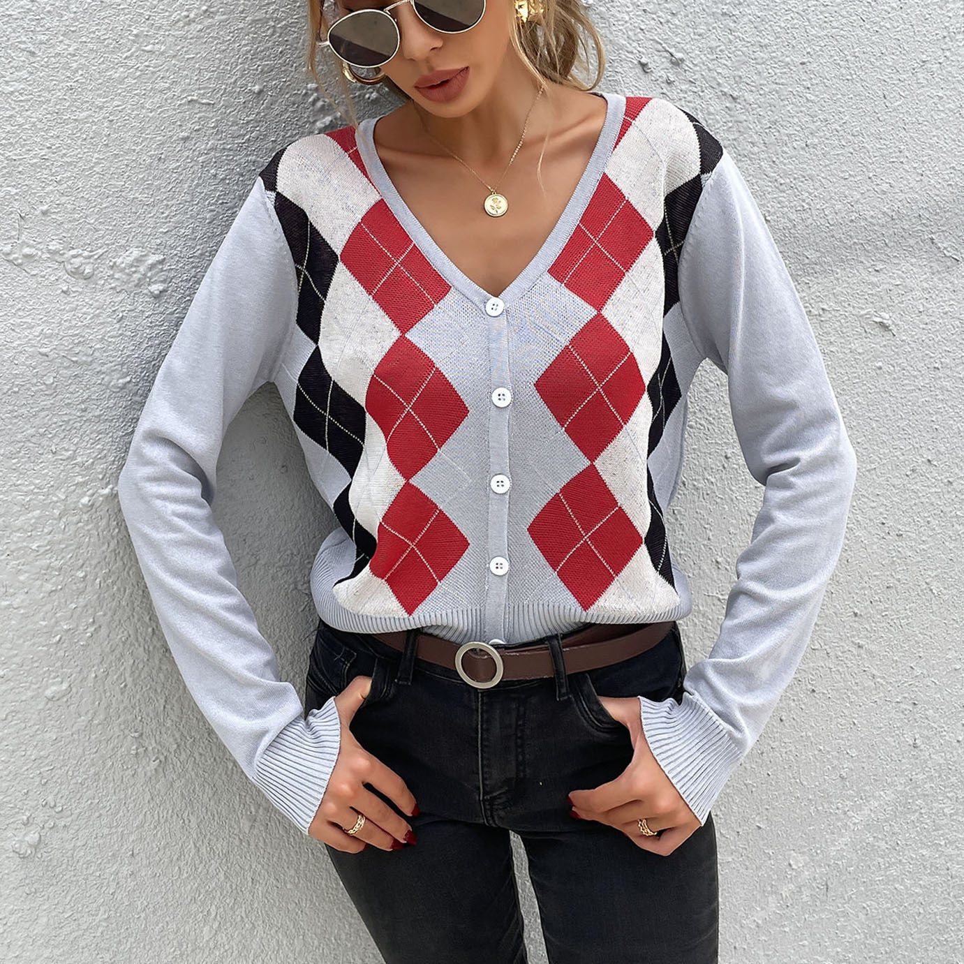 A woman wearing argyle cardigan in gray with red diamonds, styled with sunglasses, gold jewelry and black jeans