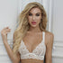 Model wearing white lace bralette, posing against white paneled wall, blonde hair styled in waves, direct face-on portrait shot