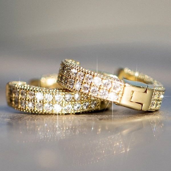 Two gold tone crystal-encrusted hinged bangle bracelets with clasp closure, sparkling against dark surface, showing detailed pave setting