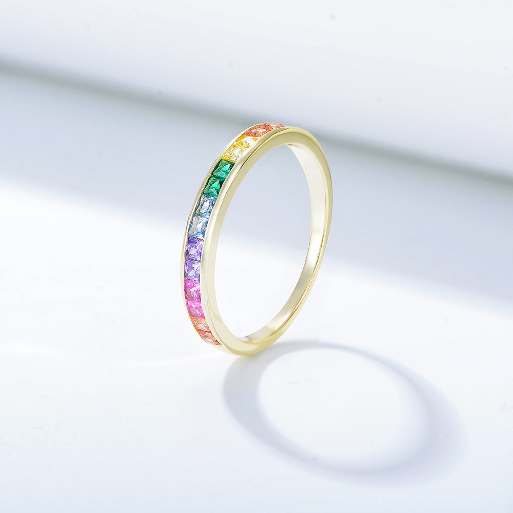 A gold rainbow eternity band with channel-set multicolored gemstones arranged in ROYGBIV order on white surface