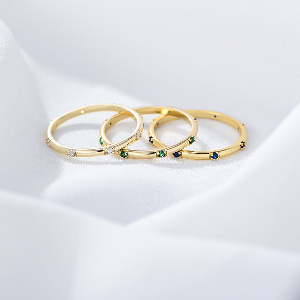 Three delicate gold rings with different gemstones - diamonds, emeralds, and sapphires against white background